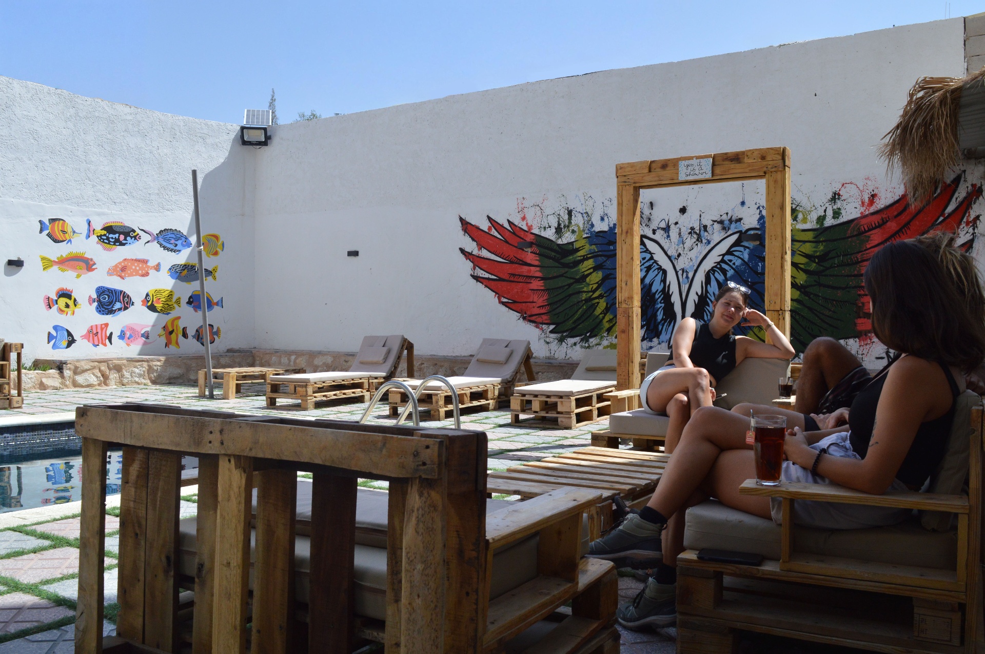 Guests relaxing with drinks by the pool under the wings mural