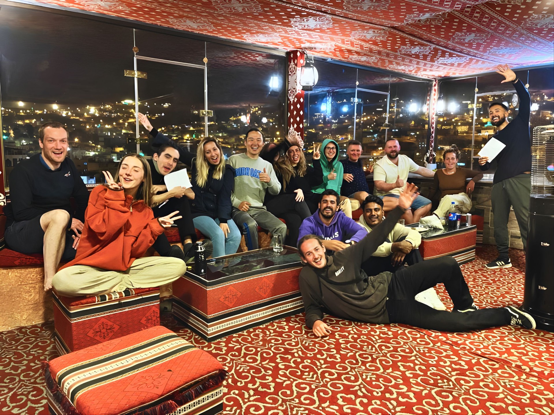 Group of backpackers laughing on the rooftop at night with Wadi Musa city lights