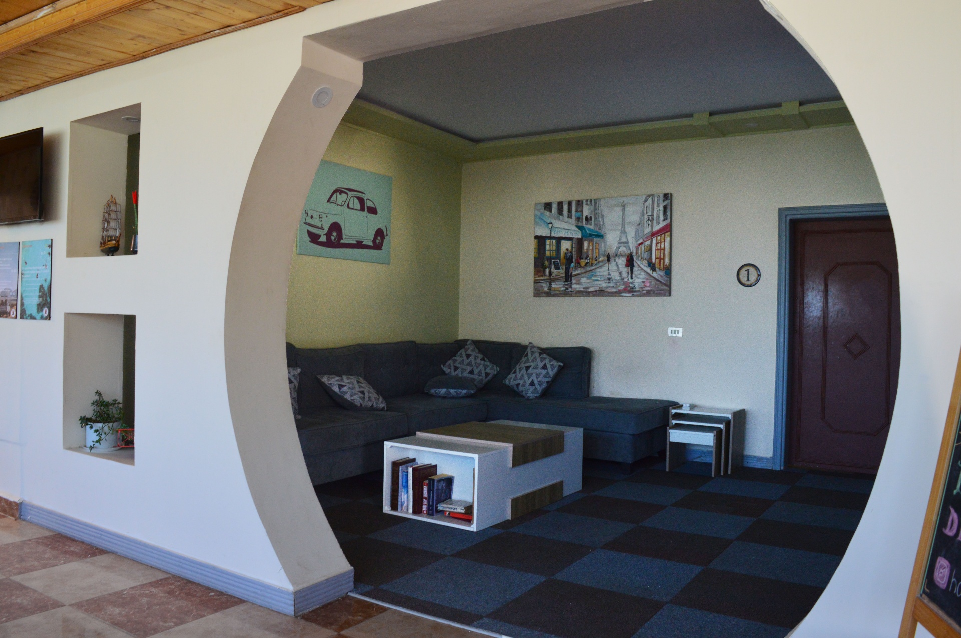 Common TV lounge with grey sofas and bookshelf seen through an arch